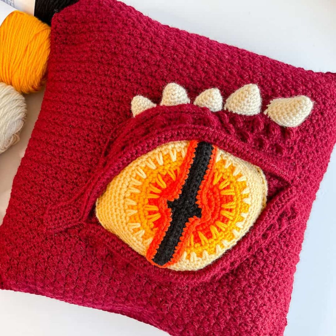Crocheted dragon eye pillow with a dragon eye design on a white background