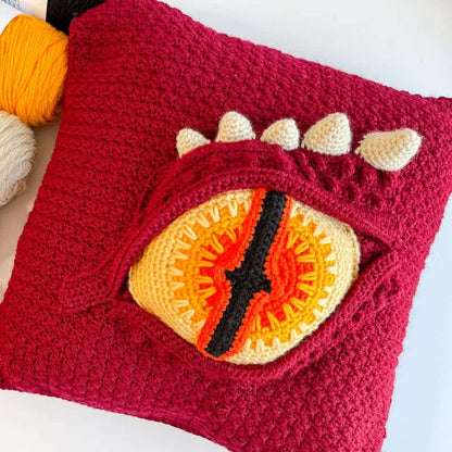 Crocheted dragon eye pillow with a dragon eye design on a white background
