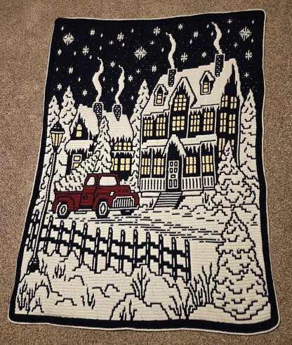 Handmade christmas crochet blanket with festive winter village on a brown surface