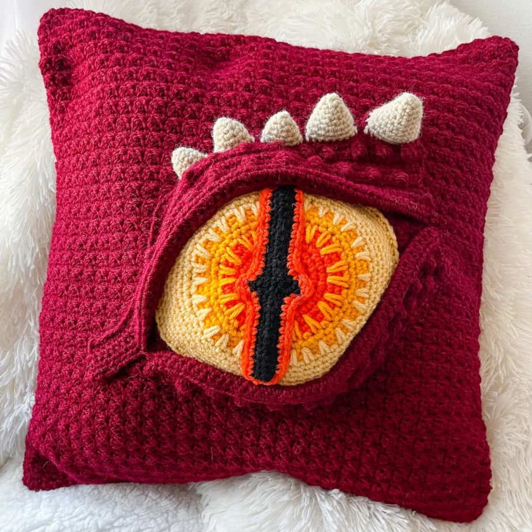 Crocheted pillow with a dragon eye design on a white fluffy surface