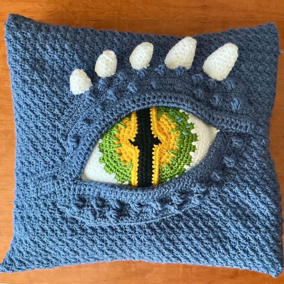 crocheted blue dragon eye pillow handmade gothic pillow on a wooden surface