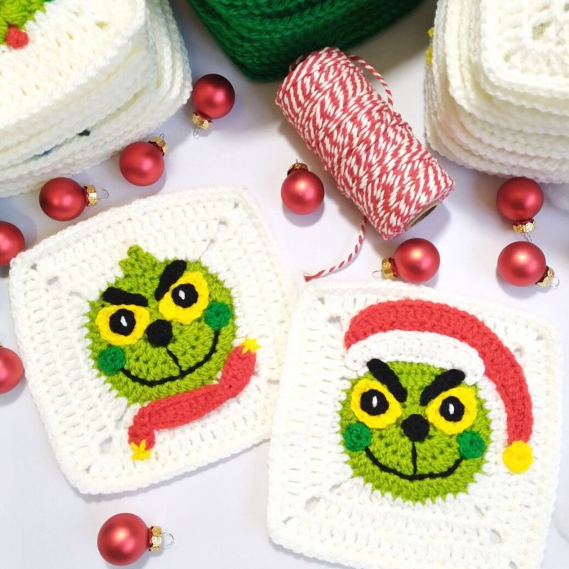 Two crocheted granny squares with Grinch faces surrounded by Christmas decorations on a white background.