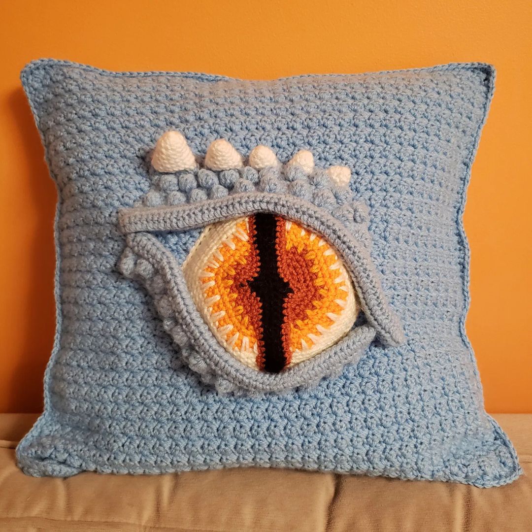 Crocheted pillow with a dragon eye design on an orange background