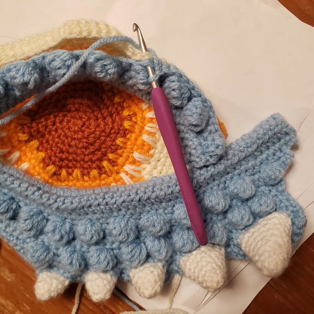 unfinished Crocheted dragon eye pillow with a purple hook on a wooden surface