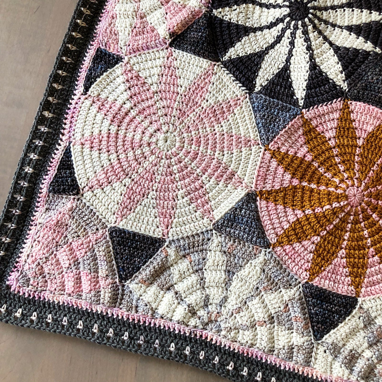 Close-up of a crocheted marguerite blanket with geometric patterns in pink, black, and brown.