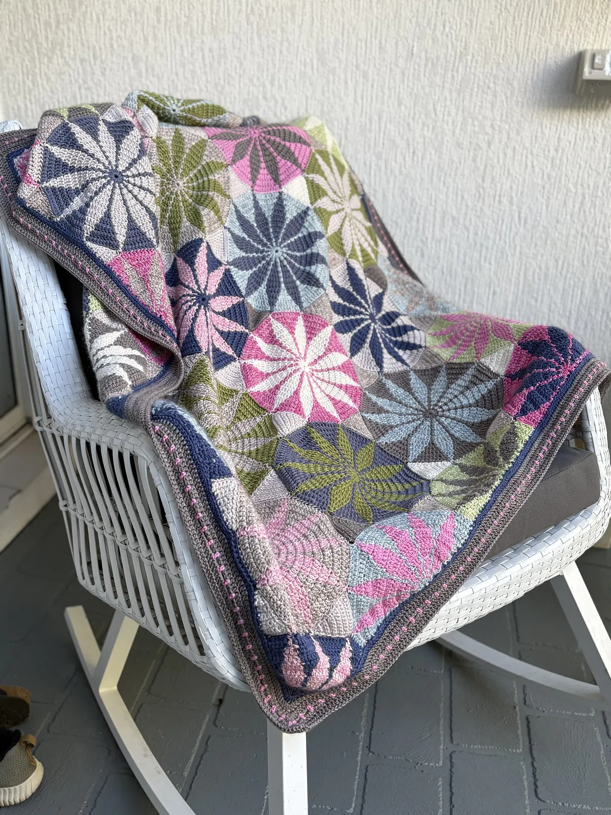 Colorful crocheted marguerite blanket with geometric patterns draped over a white chair.