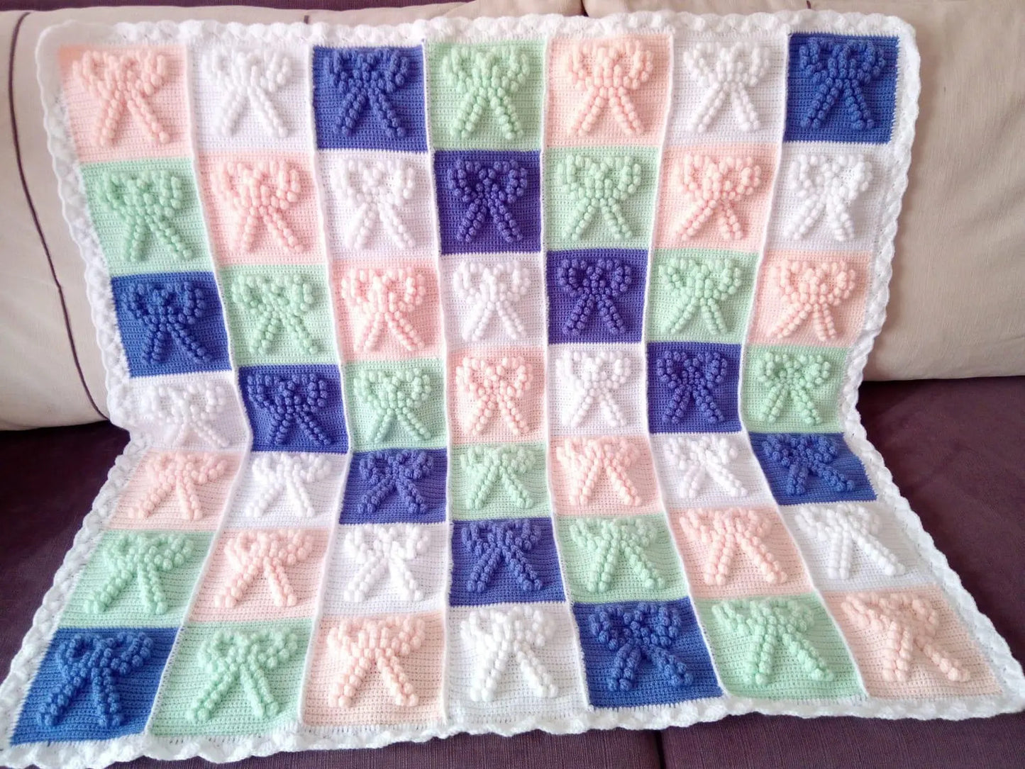 Crocheted blanket with bow pattern in pastel colors on a couch.